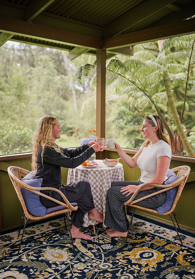 Two women sharing tea and conversation in the sanctuary’s open-air lanai surrounded by tropical plants.