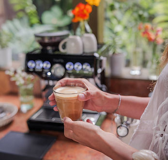 Guest enjoying a freshly made latte inside the Heart House café kitchen at Hamakua Sanctuary, surrounded by tropical light and flowers.