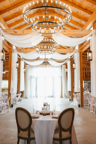 Rustic barn wedding reception at Cedar Hills Farm near Chattanooga, TN with wood beams, white draping, round chandeliers, and elegantly set tables