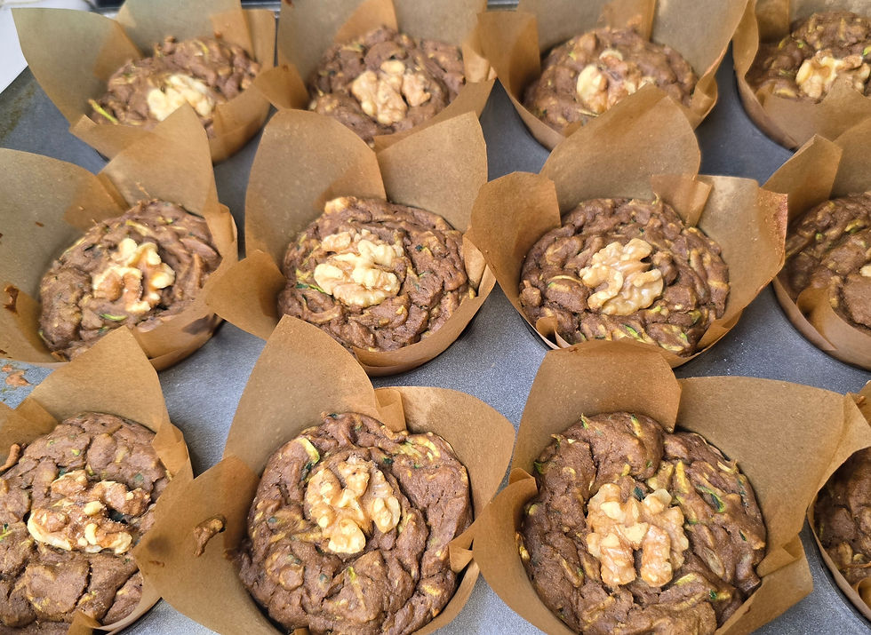 A muffin tin filled with freshly baked spiced zucchini walnut muffins in brown tulip paper liners, each topped with a whole walnut half.