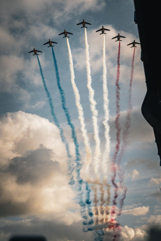 Avions de la Patrouille de France volant en formation avec traînées de fumée tricolores dans le ciel.