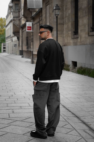 Jeune homme portant une tenue streetwear marchant dans la rue, photographié en extérieur dans un environnement urbain.