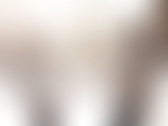 A couple in winter clothes playfully interacts in falling snow, backlit by sunlight. They smile warmly in a snowy park setting.