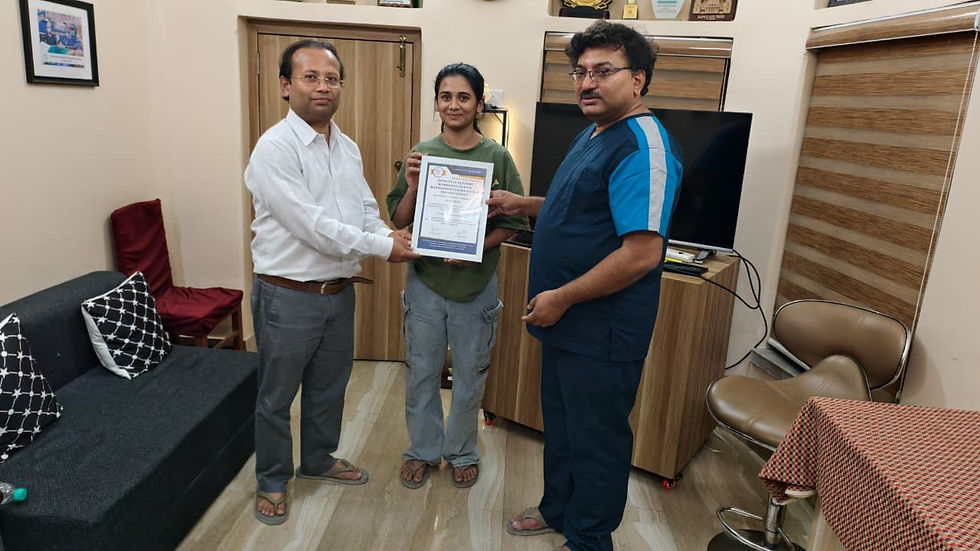 Three people stand in an office, holding a certificate. One wears a white shirt, another in green, and the third in blue. Awards adorn the wall.