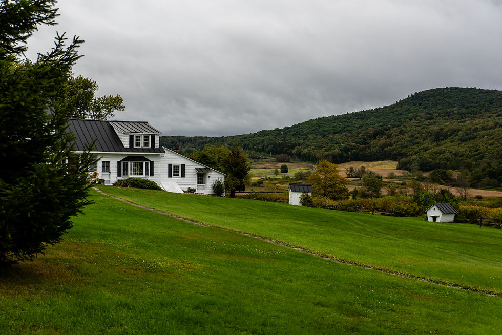 A white country farmhouse sits on a lush, green lawn overlooking the NC mountains.