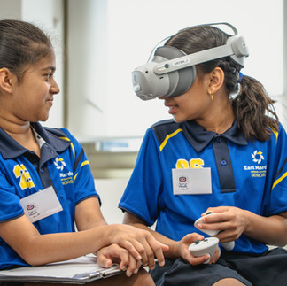 Two primary school students facing each other, one us using a VR headset and controller.