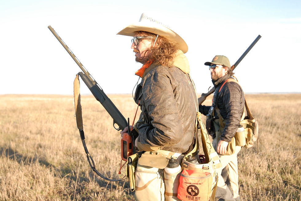 Two hunters walking through an open grass field carrying shotguns during an upland hunt.