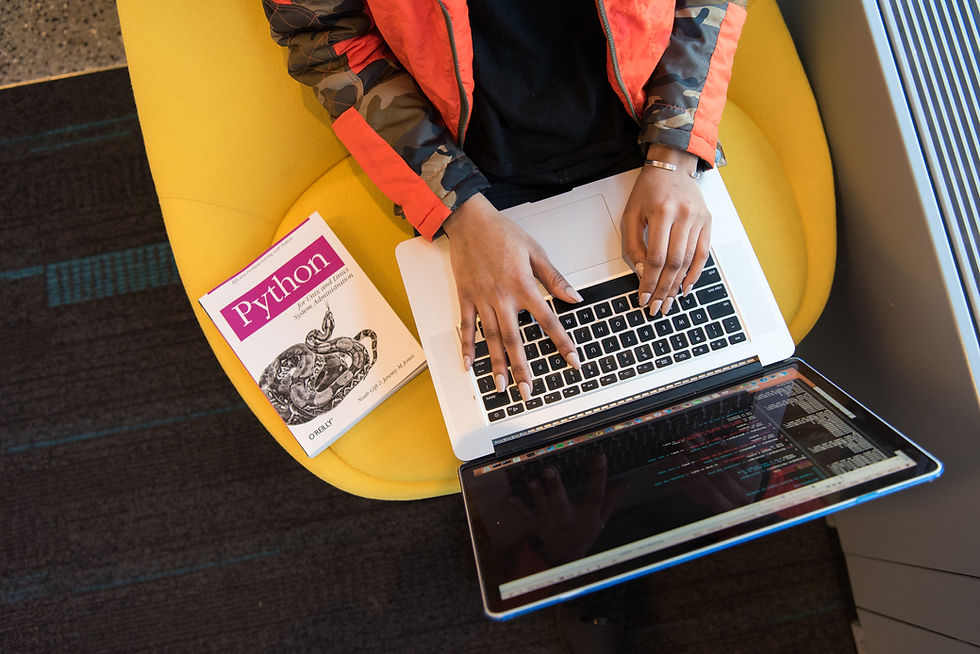 Woman coding on her laptop with a book titled "Python" next to her