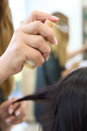Hair stylist applying finishing spray to a client’s hair inside Poshed Beauty Bar