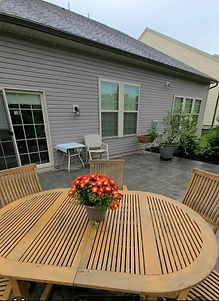 Paved patio with wooden dining set and house in background