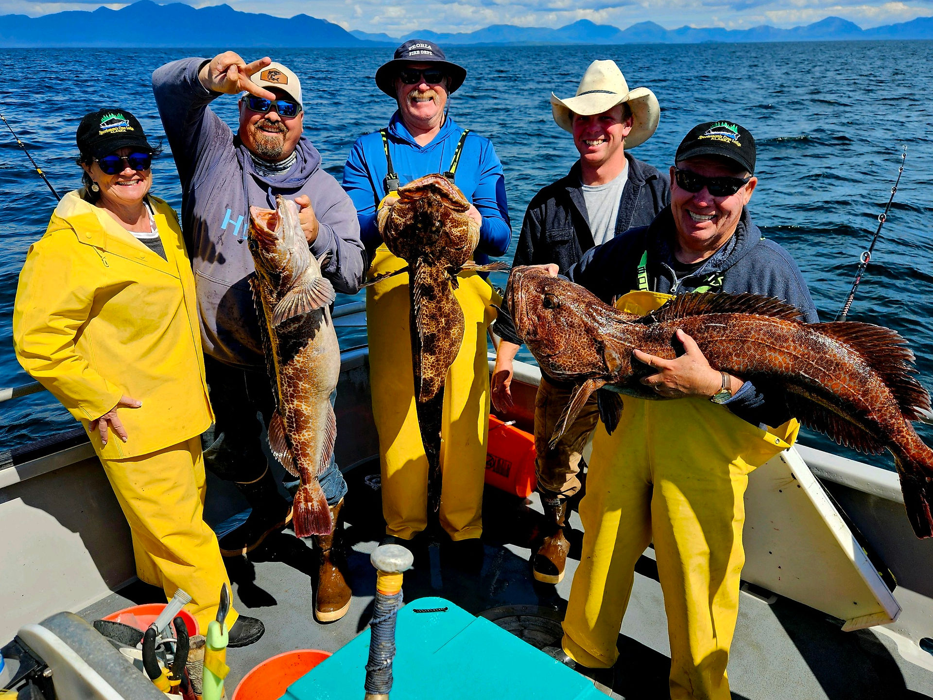 a group of 5 male fisherman holding up their massive lingcods they caught while deep sea fishing in alaska on board a sportsmans cove boat