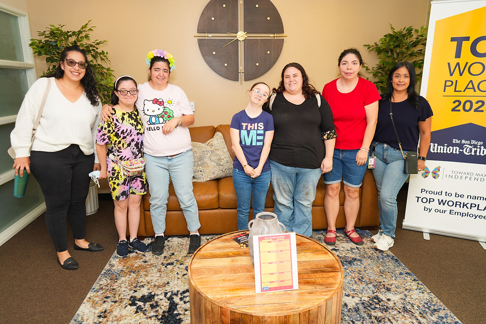 Six smiling people stand indoors near a "Top Workplace 2023" banner. A round wooden table and modern clock decorate the cozy room.