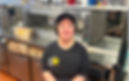 Smiling woman in black cap and shirt with star logo sits in a restaurant kitchen beside a drive-thru/dine-in counter.