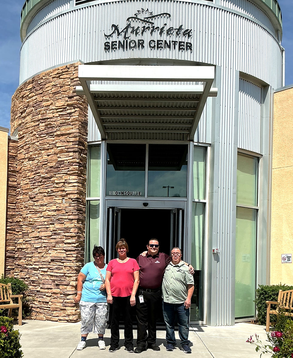 Four adults pose outside Marietta Senior Center entrance with stone and metal facade; Town Square visible on glass.