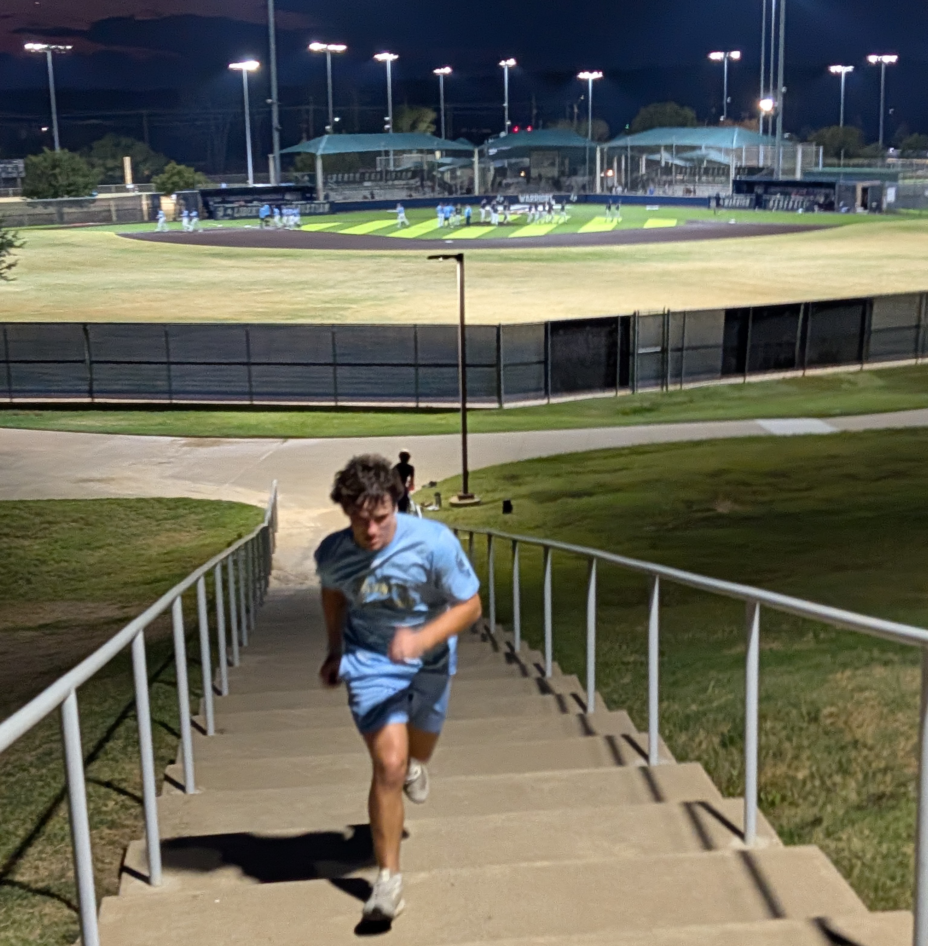 A youth athlete runs stairs at night under the lights, putting in off-season work.