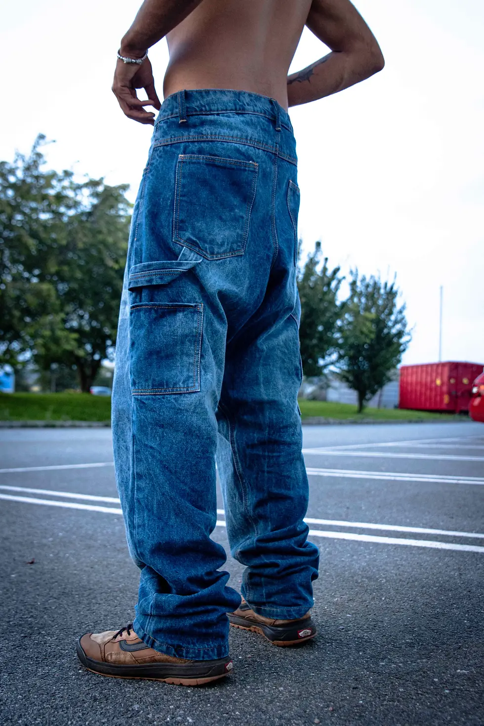 Side view of baggy blue jeans in a parking lot, with trees in the background.
