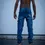 Thumbnail: Back view of a person wearing blue jeans with a yellow patch, standing against a wall.