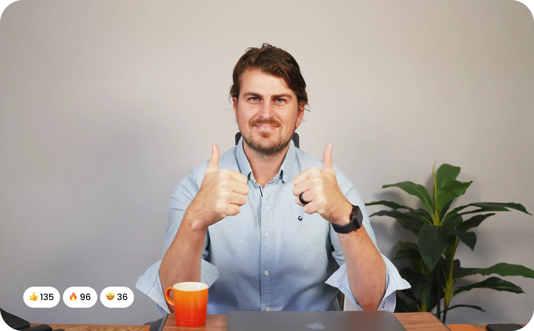 Image of Kyle Prinsloo making a thumbs up gesture with both hands while sitting at his desk with a laptop and coffee cup