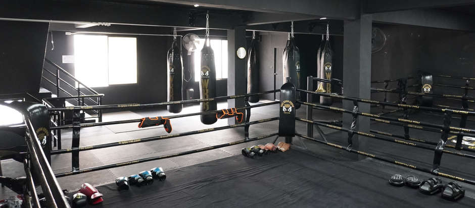 WKK Muay Thai Fighter Gym with 2 boxing rings and 6 heavy bags in teh background. WKK Gym logos and branding.
