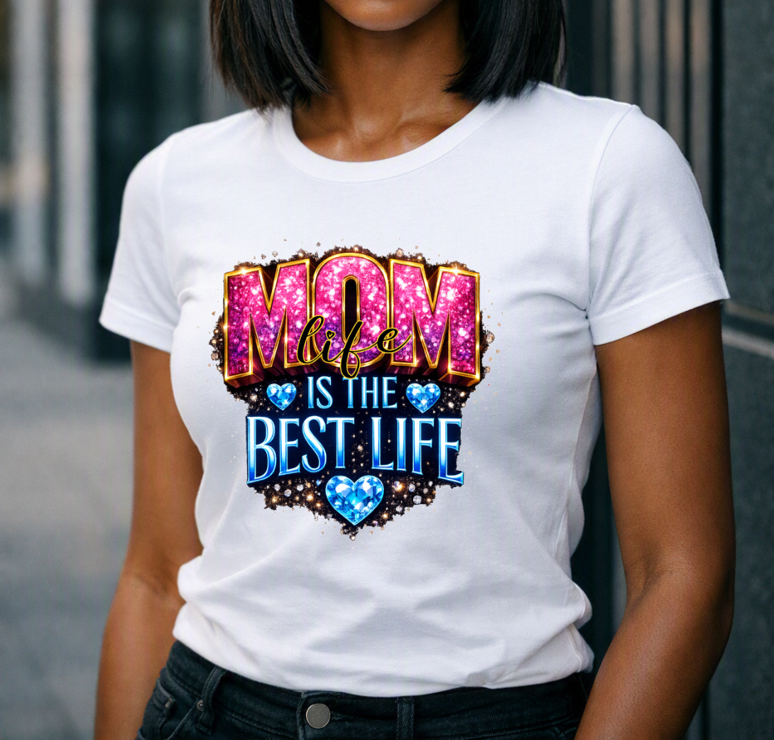 A white shirt featuring a sparkling pink and blue βMom Life Is the Best Lifeβ design with blue heart accents