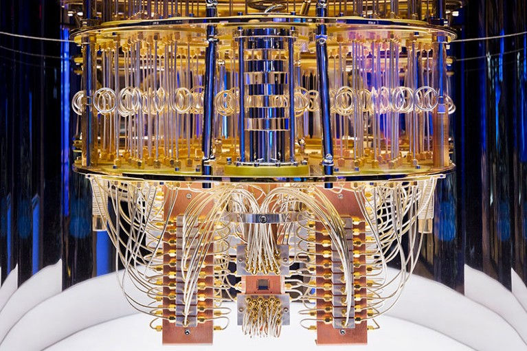 Close-up of a quantum computer chandelier with intricate gold wiring and rods, set in a reflective, modern environment with blue lighting.