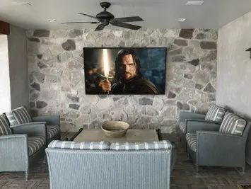 Outdoor TV mounted on stone rock wall in backyard entertainment space in Purchase New York.