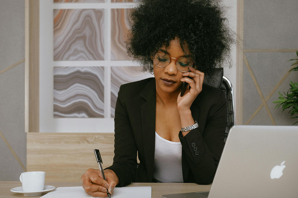 Photo of a lady on the phone and making notes, sitting next to her laptop.