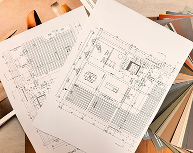 Piantina tecnica di un appartamento su tavolo da disegno circondata da campioni di materiali, finiture in legno e tessuti per
