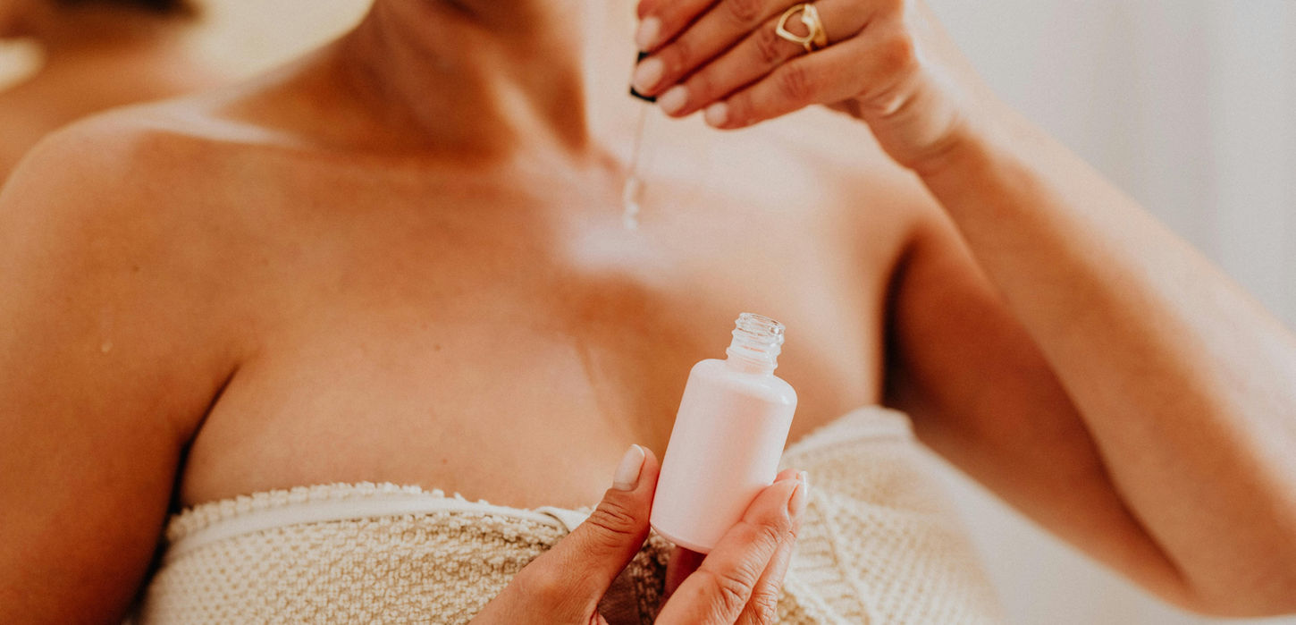 Woman applying pink serum to her chest after chemical peel at Beauty Queens Aesthetics & Wellness Medicine
