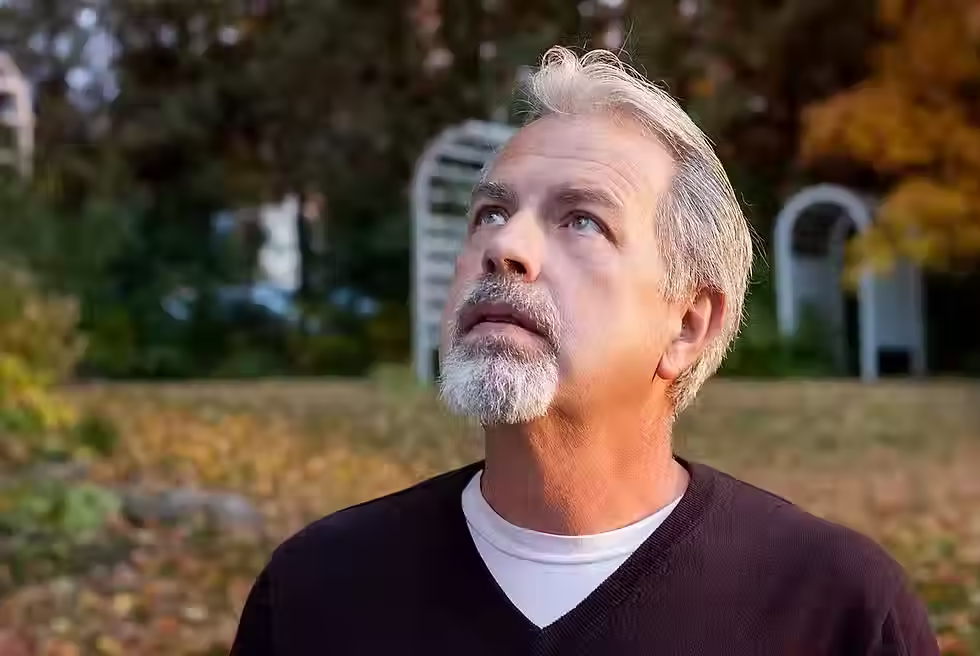 Man outdoors in a wooded area looking upward with a focused expression, suggesting attentiveness during a paranormal or intuitive moment.