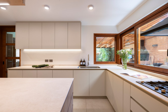 Cocina a medida en tonos claros con isla central, detalles en madera, vitrina iluminada y mobiliario integrado de piso a cielo.
