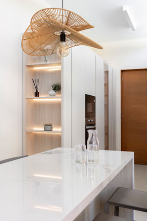 Cocina a medida en tonos claros con isla central en acabado Calacatta, vitrinas iluminadas, detalles en madera y mobiliario integrado de líneas minimalistas.