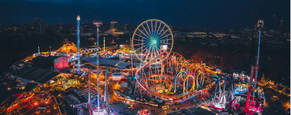 Aerial view of a brightly lit amusement park at night with rollercoasters, Ferris wheel.