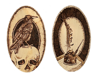 Two wooden oval plaques side by side on white background. The left one shows a pyrography drawing of a raven perched on top of a human skull. The right plaque shows a quill sticking out of an inkwell.