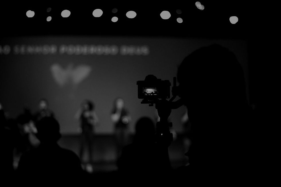 Equipe de mídia fazendo registro do culto. No palco, pessoas cantando.