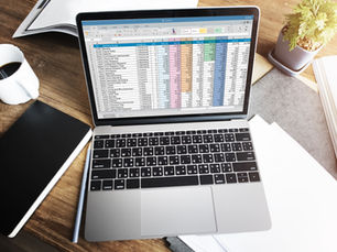 Mesa com xícara de café, caderno, papéis e notebook aberto em uma planilha