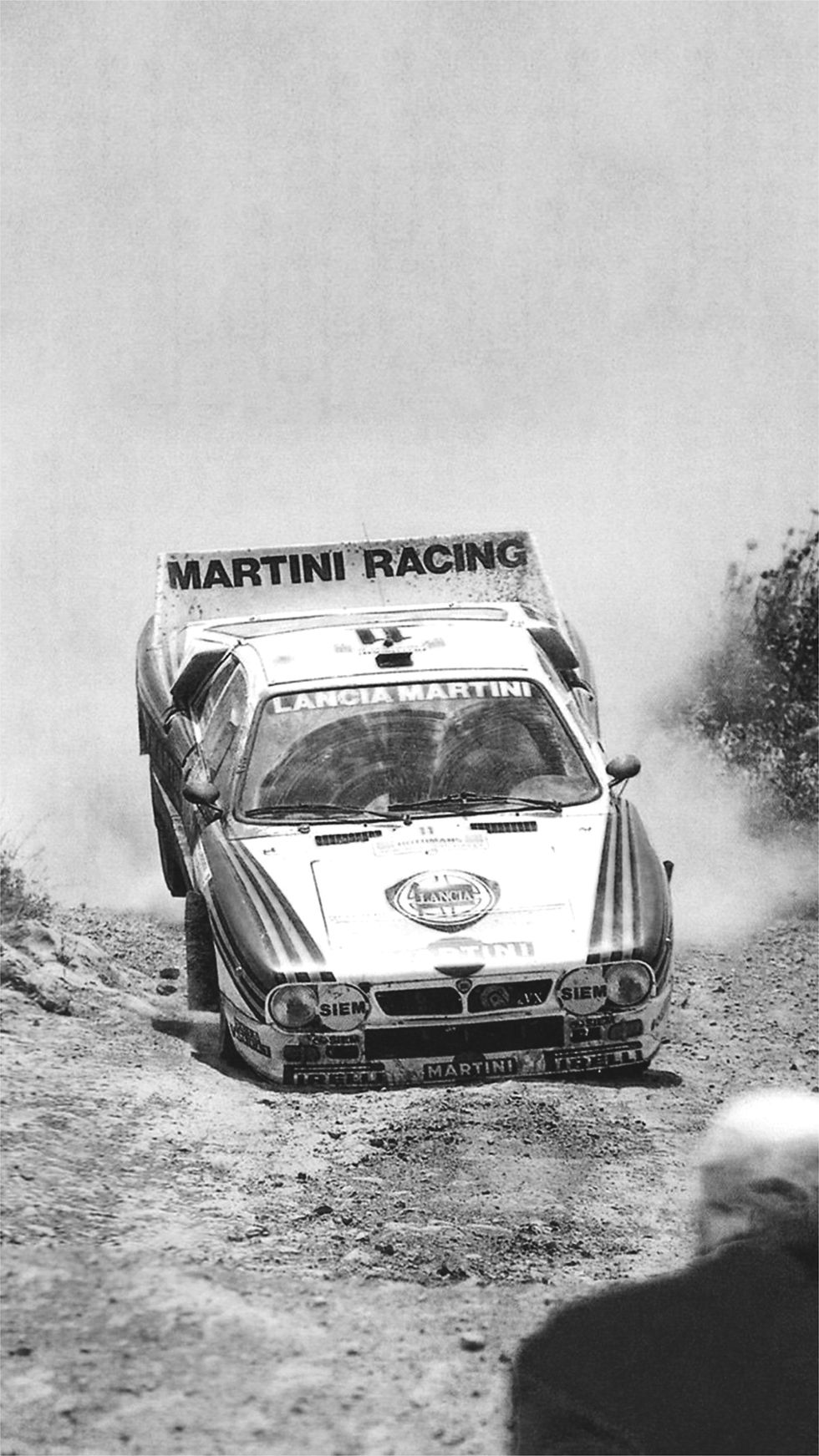 Lancia 037 bei der Gruppe B Rallye. Im Hintergrund sieht man Menschen und aufgewirbelten Staub.