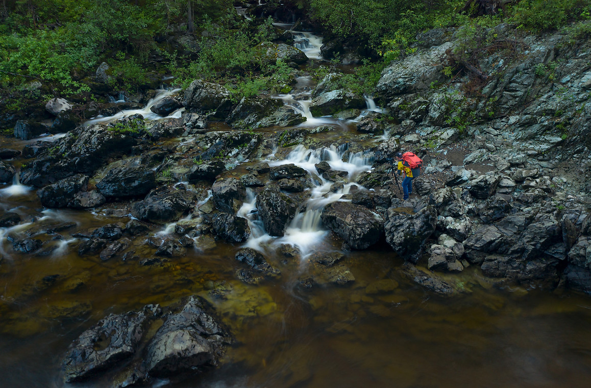 A photographer with his camera setup over a beautiful stream leading into the Willow River in the fall