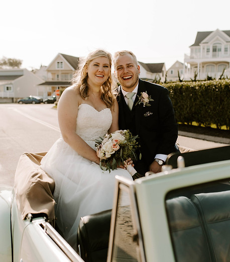 couple sitting on the back of a convertible as bride holds her bouquet