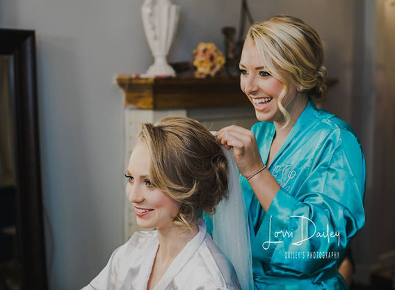 Smiling bridesmaid in a blue robe helping bride with veil