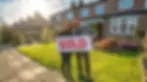 Happy couple celebrates successful property investment, holding sold sign outside their new real estate investment - first step to investing in property