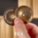a bronze and chromium jingle held between a finger and thumb