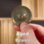 a single aged brass jingle held between a finger and thumb
