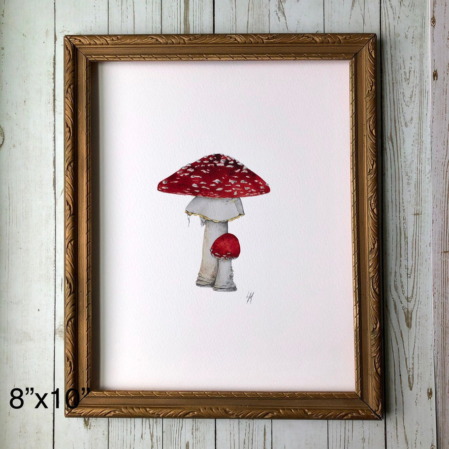 art print of watercolor depicting whimsical red and white toadstool mushrooms on white paper in frame