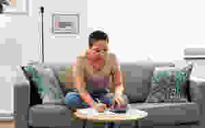 Female with short hair earing glasses sitting on sofa writing and using a calculator