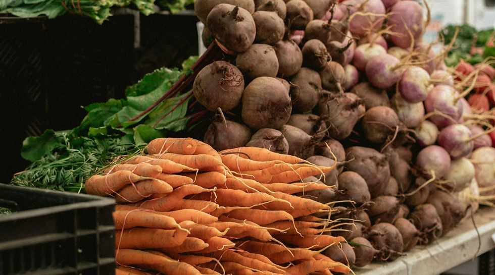 Fresh carrots, beets, and turnips stacked in a market setting. Vibrant greens and purples create a natural, earthy atmosphere.
