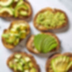 Toasted bread topped with sliced, diced, and mashed avocado on a marble surface. Varied textures and vibrant green color.