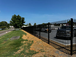 A black metal pole fence surrounding a parking lot on a grassy hill