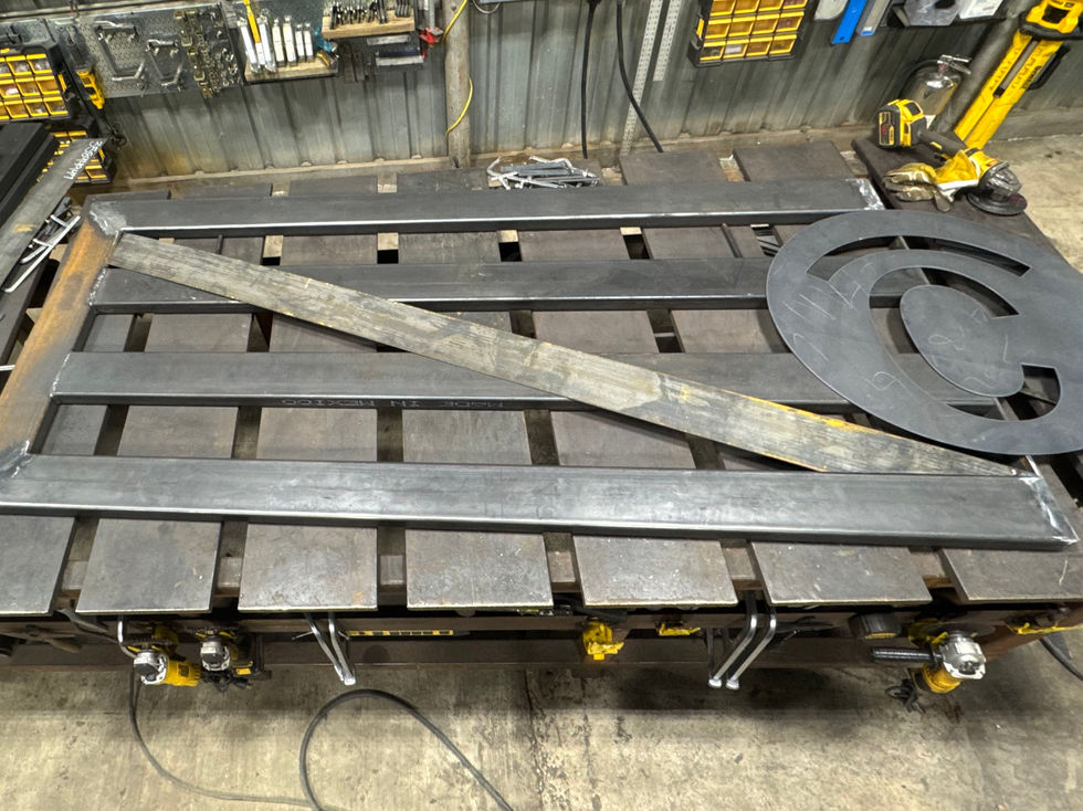 A metal workbench with a custom gate and a large circular metal logo laid out on top, surrounded by clamps, tools, and workshop equipment—perfect for custom fabrication projects like custom gates.