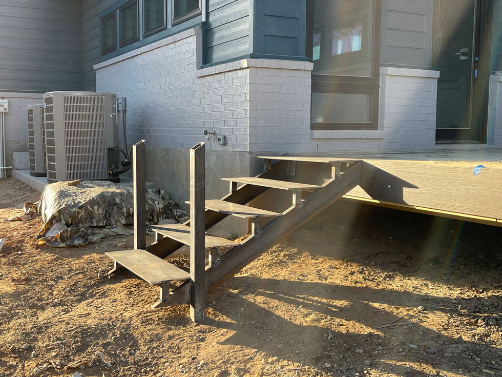 A set of unfinished custom stairs leads up to the back porch of a gray house. The area around the steps is bare dirt, and an air conditioning unit and a covered pile of materials are nearby.